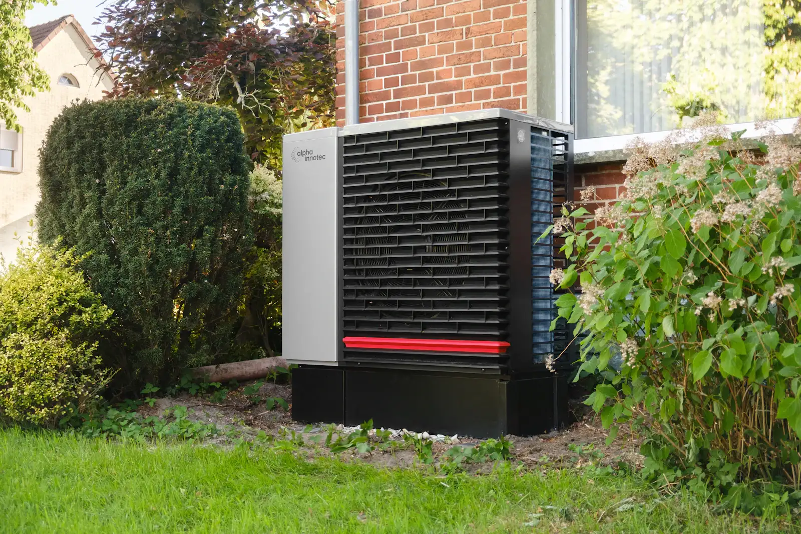 An air source heat pump unit in a garden beside a brick house