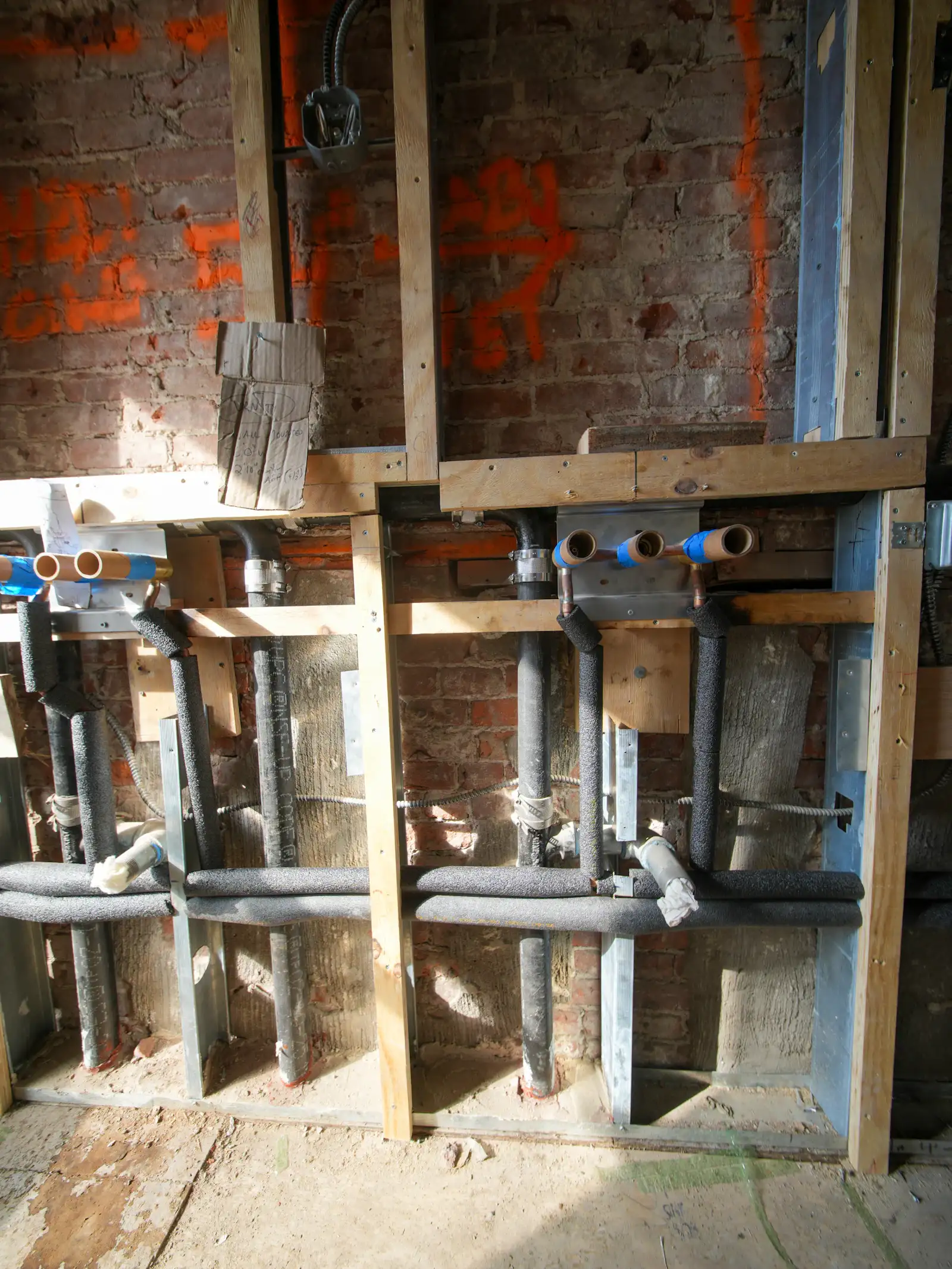 Insulated hot and cold water pipes being fitted into a stud wall during a renovation