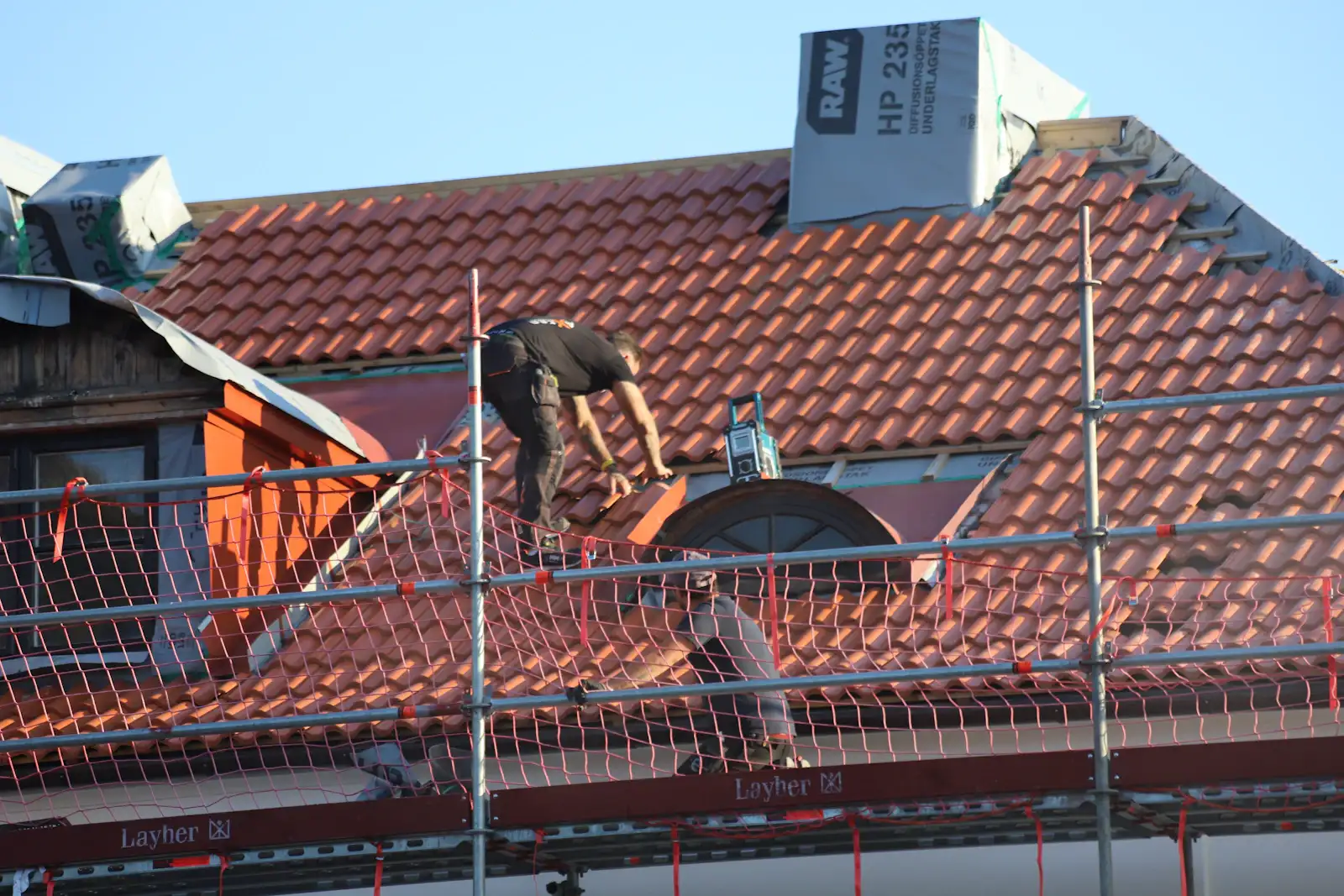 A roofer working on a clay tiled roof from scaffolding