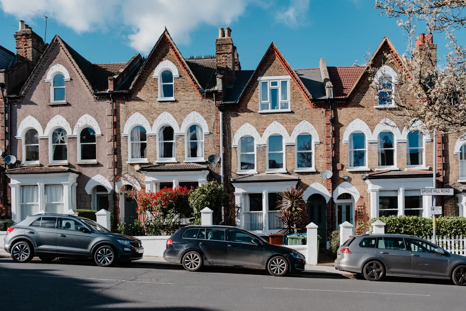 A row of Victorian terraced houses with bay windows and cars parked outside